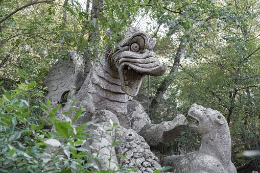 Bomarzo, Italy - 10 08 2023: Dragon figure sculptured in giant rocks in Bomarzo Sacro Bosco Park in Italy