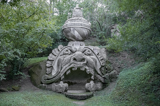 Bomarzo, Italy - 10 08 2023: Head figure with open mouth entrance sculptured in giant rocks in Bomarzo Sacro Bosco Park in Italy