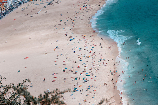 Crowd of people on a sandy beach of the Atlantic ocean in Portugal during the summer. Panoramic shot from a hill (not drone shot).