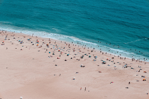 Crowd of people on a sandy beach of the Atlantic ocean in Portugal during the summer. Panoramic shot from a hill (not drone shot).