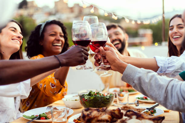 Young group of people enjoying dinner reunion in the evening at rooftop home. Young group of people enjoying dinner reunion in the evening at rooftop home. Millennial diverse friends social gathering reunited on terrace table, having fun celebrating barbecue party at night. big family table stock pictures, royalty-free photos & images