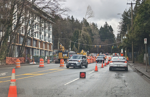 Surrey, Canada - March 2, 2024: Looking east as traffic navigates between lines of safety cones on the 13900-block of 96th Avenue near 140th Street. Background shows the Green Timbers Urban Forest Park. Winter morning in Metro Vancouver.