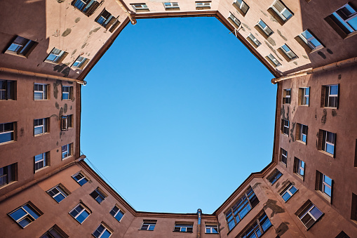 Bottom up view of old octagon courtyard well in St. Petersburg, Russia. Wall, windows and part of blue sky