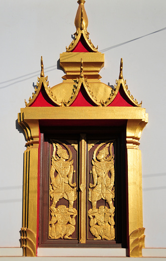 Vientiane, Laos: Wat That Luang Tai, temple on That Luang Park, Pha That Luang complex, Ban Thatluang. Ornate wood carved doors framed in gold and red, with miniature roofs bearing chofa finials.