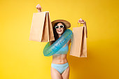 young curly girl in a blue swimsuit with an inflatable swim ring on a shopping spree holds a lot of shopping bags