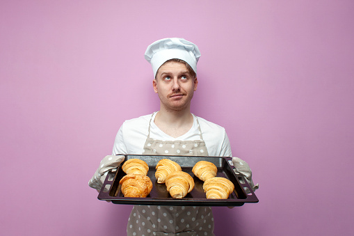 Nice young female baker with a baking sheet of freshly baked buns.
