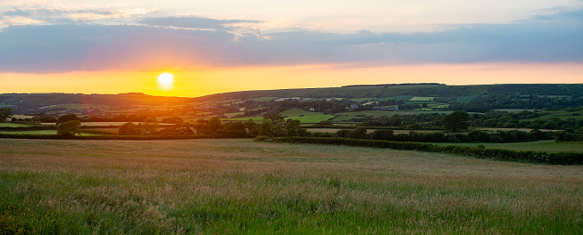 A sunset photographed over farmland, crops and low lying hills in Dorset, UK, close to the historic Corfe Castle.