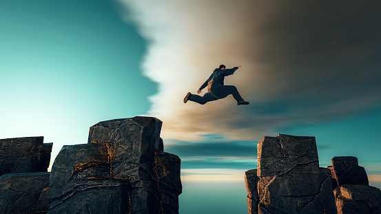 Concept of determination, adrenaline and over coming fear. Man jumps from one rock formation to another. It is a dangerous jump and he uses all of his speed and strenght to make it across.