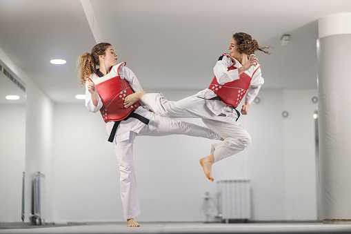 Taekwondo athletes wearing doboks are practicing combat at martial art school.