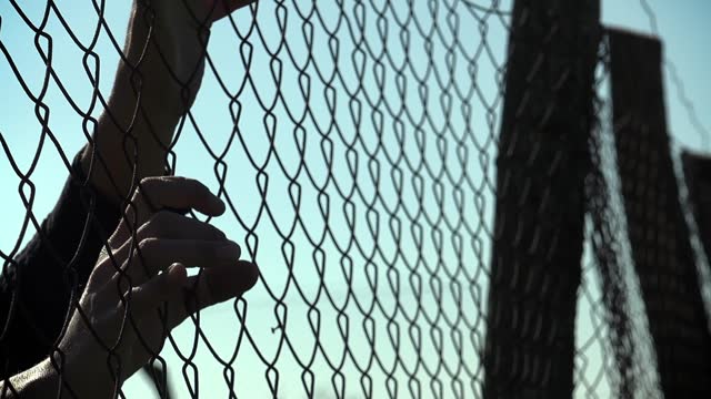 hopeful woman's hands clinging to the border fence: dreaming of freedom, peace
