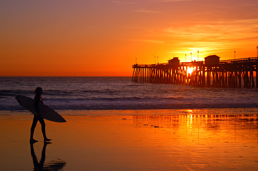 San Clemente, CA, USA November 5 A surfer carries his surfboard back from the ocean as the sun sets behind the pier in San Clemente, California