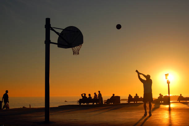 Laguna Beach, CA, USA November 6 An adult man takes a shot at a basketball court in a park near the shore in Laguna Beach, California, as the sunset renders him in silhouette