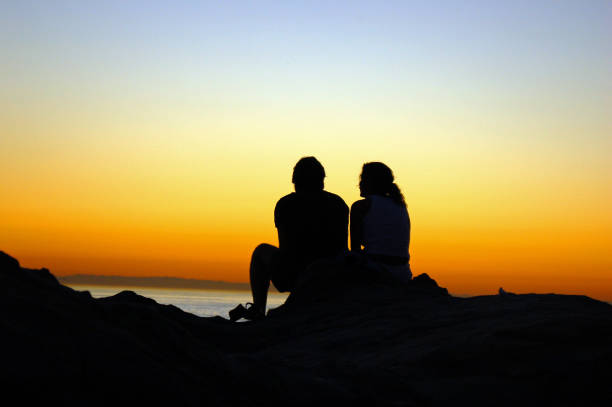 Laguna Beach, CA, USA November 6, A young couple looks out to the sea as the sunset sky renders them in silhouette on the rocky coast of Laguna Beach, California