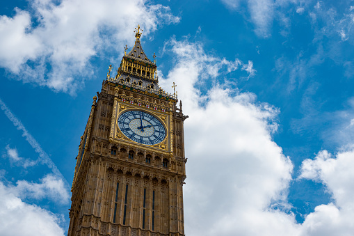 LOW ANGLE VIEW, CLOSE UP: Famous Big Ben with its exact clock and gilded accents against a partly cloudy blue sky. Exquisitely finished details on iconic cultural symbol of United Kingdom in London.