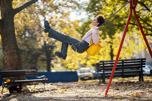 A carefree stylish girl is swinging on a swing in city park.
