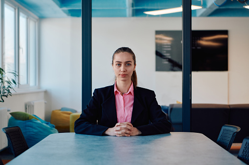 Successful young female leader in a suit with a pink shirt sitting in a modern glass office with a determined smile
