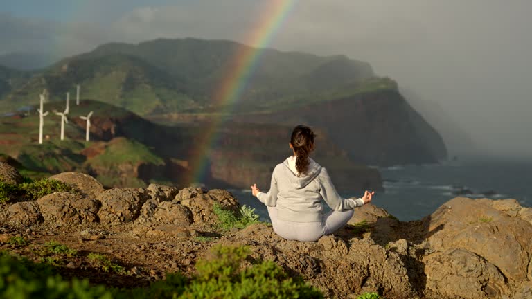 Yoga at sunrise with rainbow and wind turbines.