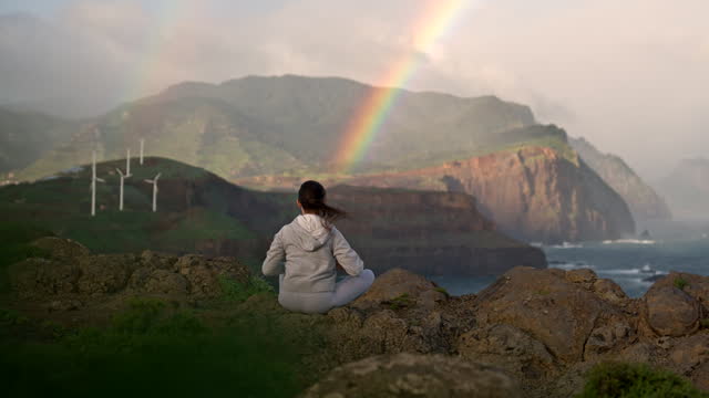 Yoga at sunrise with rainbow and wind turbines.