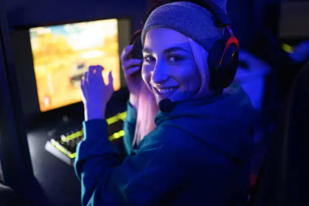 Close shot of a smiling woman gamer looking at the camera while playing in a multiplayer video game on a pc in a gaming club. Participating in an esport online cyber games tournament. Copy space.