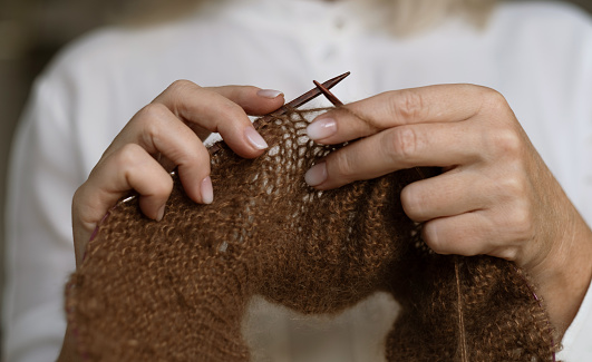 Woman's hands knitting brown wool yarn pattern. Close up picture.