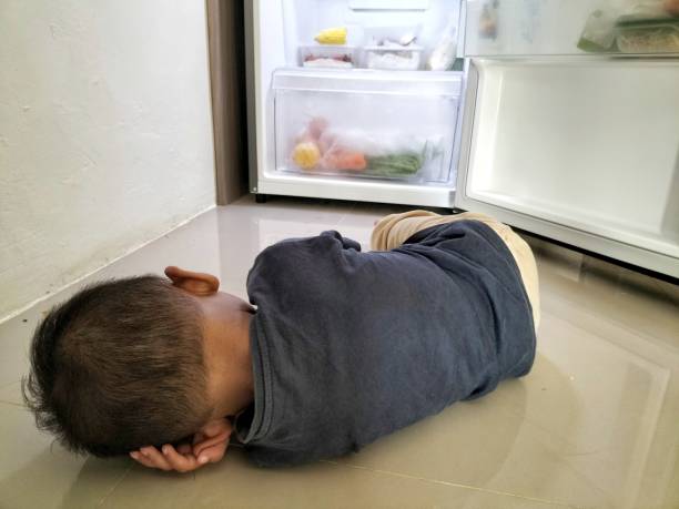 istock A boy sleeping at the floor in front of an open refrigerator. 2059480344