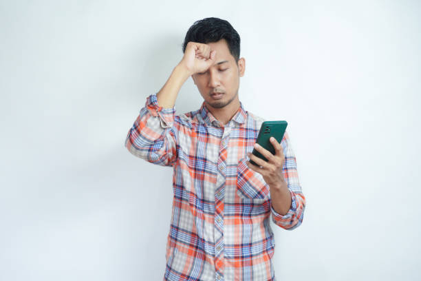 istock Asian man holding his mobile phone with sad expression 2059502074