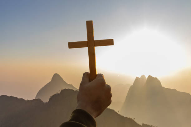 istock human hands praying to the GOD while holding a crucifix symbol with bright sunbeam on top mountains 2059546470