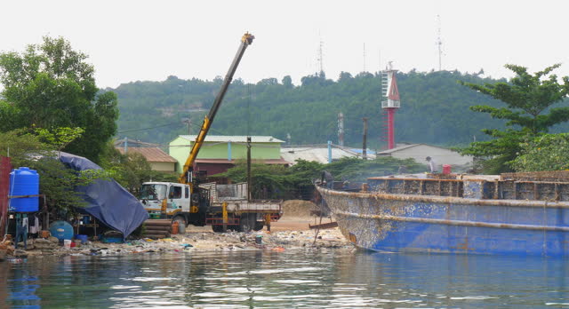 View of the bow of the cargo ship being dismantled at the water's edge.