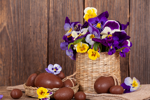 Easter chocolate eggs and pansy in a flower pot on rustic wooden table.