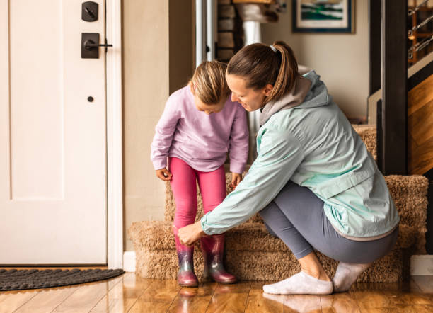 Mother helping daughter wear a raining boots.