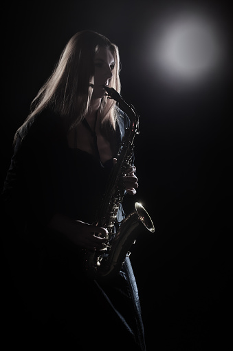 Saxophone player. Saxophonist woman playing sax. Jazz player musician in darkness