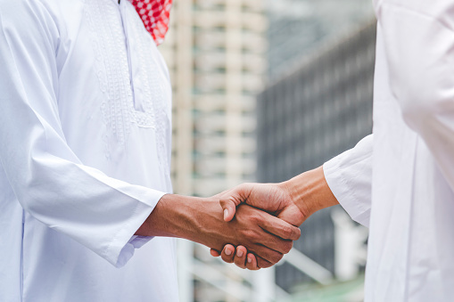 Islamic businessman shake hands together dealing success business in modern muslim UAE city. Arab man wear hijab muslim dress. Multicultural diversity business people meeting talking group cityscape