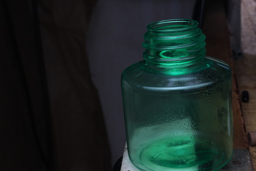 An empty transparent green 15-millimeter unbranded bottle is photographed on a black background