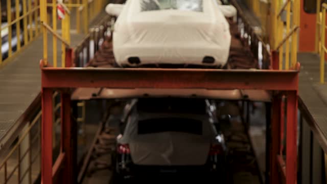 Cars on an assembly line covered in protective white wraps, in an industrial setting, shallow focus