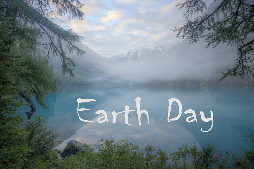 A beautiful lake in a mountain valley. The fog descends into the water. Mountain peaks with snow. Caption: Earth Day.