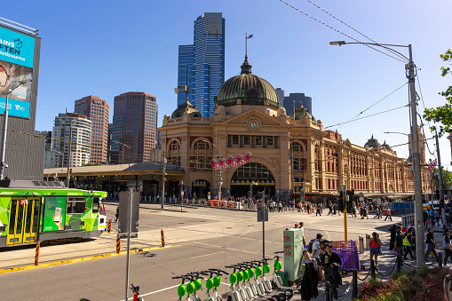 The entrance to Flinders Street Train Station in Melbourne, Australia with a traditional green tram passing in front.