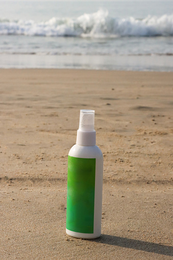 Stock photo showing close-up view of plastic bottle of mosquito repellent spray left on sandy beach.
