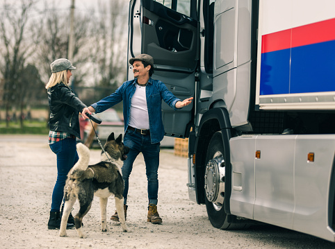 A woman truck driver comes from a trip and is greeted by her husband with a dog