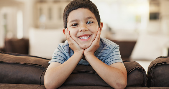 Happy, cute and face of a child on the sofa for playing, relax and weekend fun. Smile, youth and portrait of a little boy kid with an adorable expression, charming and on vacation on the couch