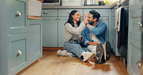Couple, coffee and sitting on floor in kitchen for quality time or fun to celebrate or discussion. Love, smile and woman with high five are bonding together with caffeine and conversation or care.