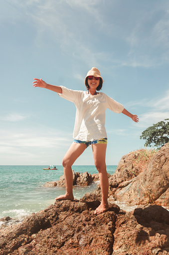 Cheerful smiling woman on cliff beach - Happy woman on the beach smiling at the camera - fun and outdoor activity. summer travel destination.