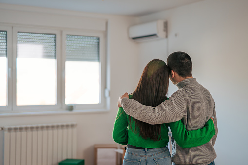 Young couple hugging and standing in front of the window in their new apartment admiring the view.
