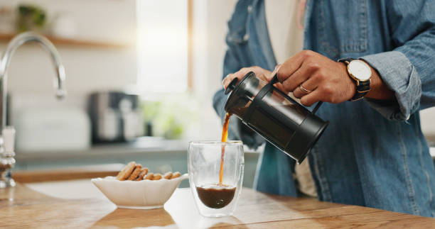 Hands, pouring coffee and breakfast in home kitchen, energy and start morning with warm matcha at table. Man, filter kettle and french press plunger for fresh organic caffeine at house for hot drink