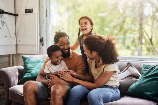 Happy African American parents enjoying with their kids on sofa in the living room.