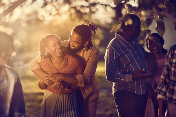 Happy embraced black couple enjoying with their family in nature at sunset.