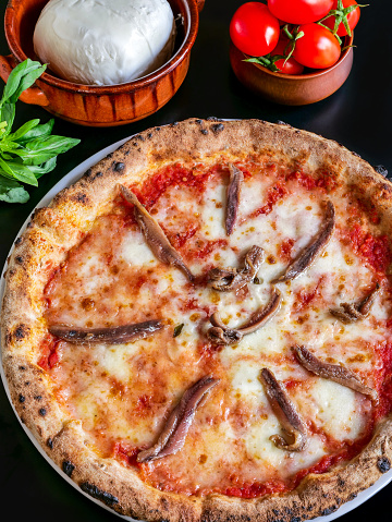 A delicious and tasty Pizza Napoletana with Italian Mozzarella, extra virgin olive oil and anchovies, rigorously cooked in a wood oven, according to the original Neapolitan tradition. In 2017 the art of Neapolitan Pizza was declared by UNESCO as an Intangible Cultural Heritage. Image in original 4:3 ratio and high definition quality.