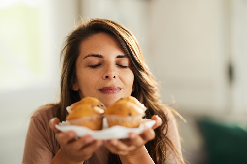 Young woman smelling fresh muffins with her eyes closed at home. Copy space.