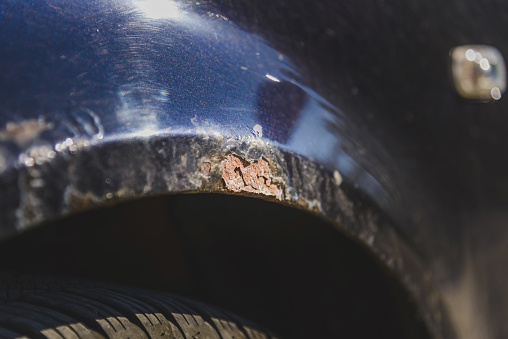 Rust on the side of blue old car. Rust hole on old worn painted metal surface.Closeup.