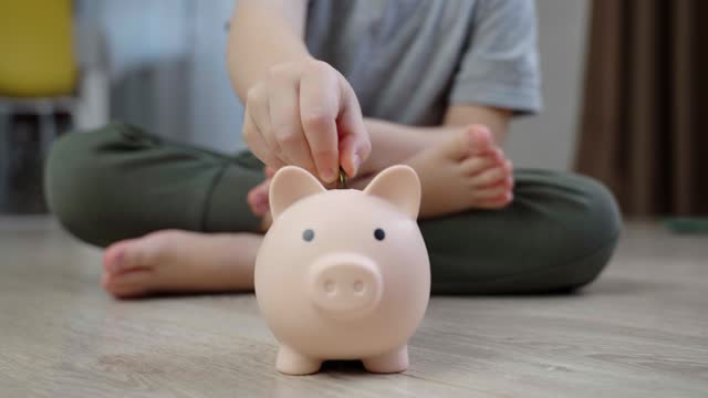 Close-up of a piggy bank on the floor into which a little boy puts coins.