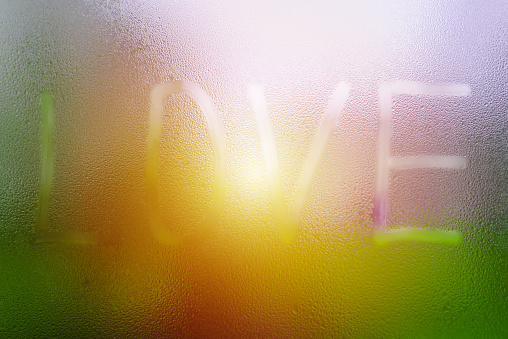 Love inscription on a dewy,foggy glass. Call for love.Selective focus.Blurred sunrise background.